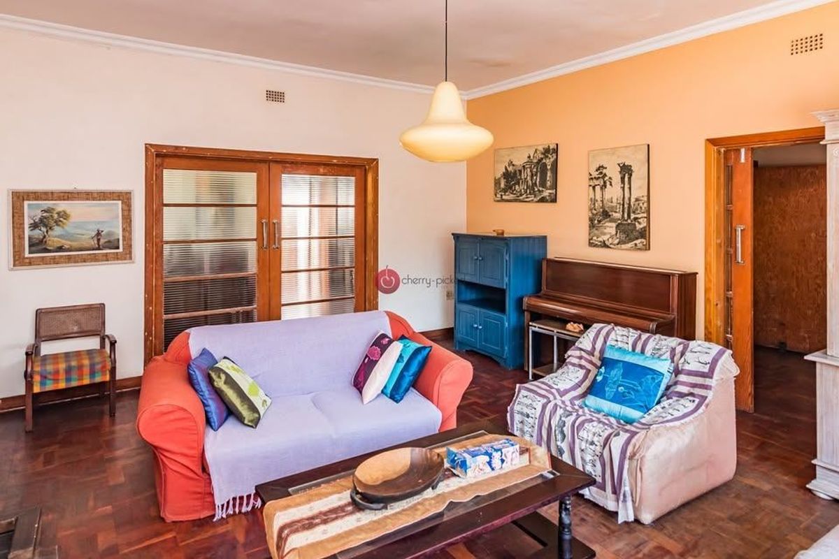 A living room featuring classic parquet flooring, timber-framed glass doors, and a central pendant light fixture, offering a warm and traditional aesthetic.