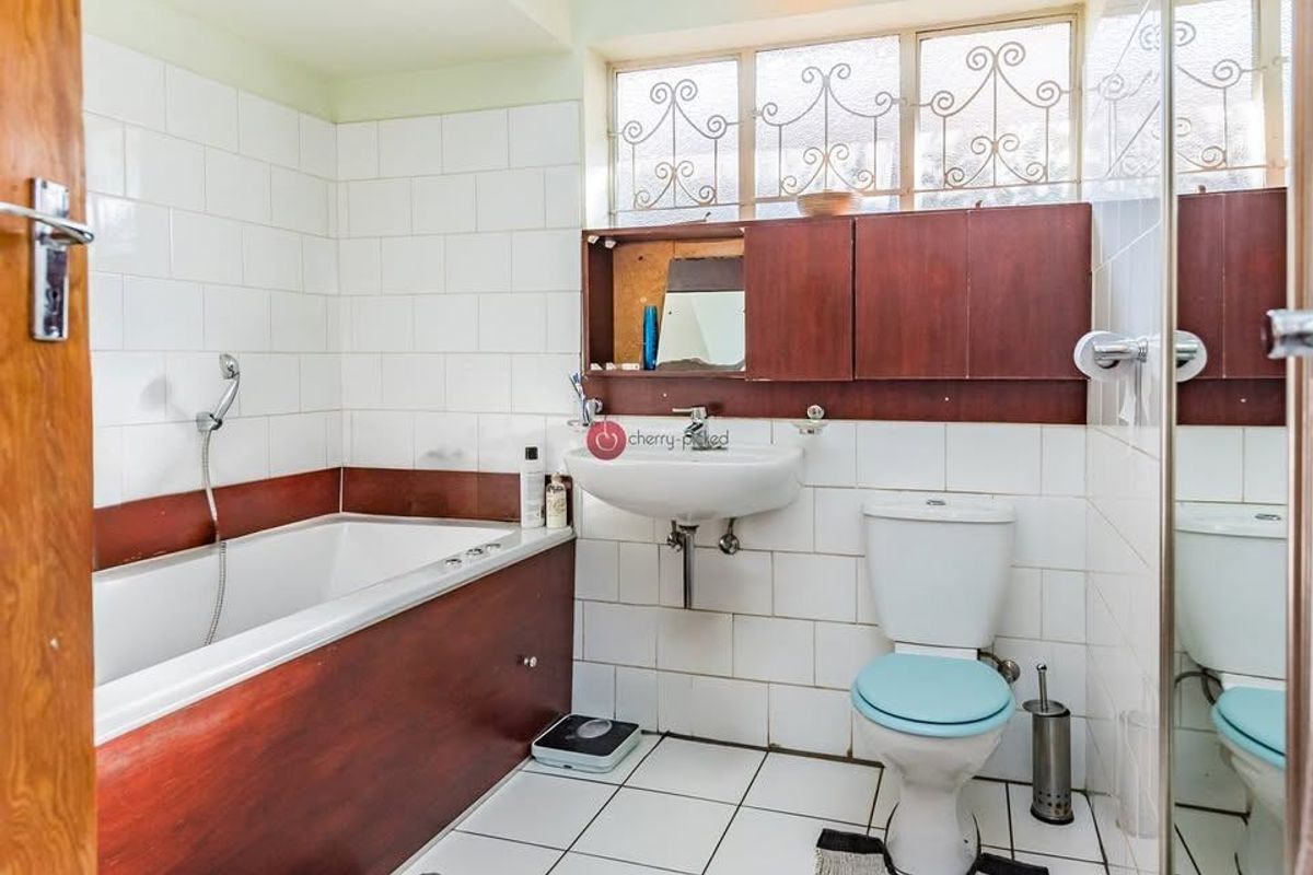 A dated bathroom featuring a bathtub, wall-mounted basin, and toilet with original tiling and cabinetry, offering significant potential for a modern renovation.