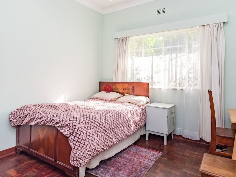 A bedroom featuring classic parquet flooring, neutral wall finishes, and a large window with security bars, providing natural light.