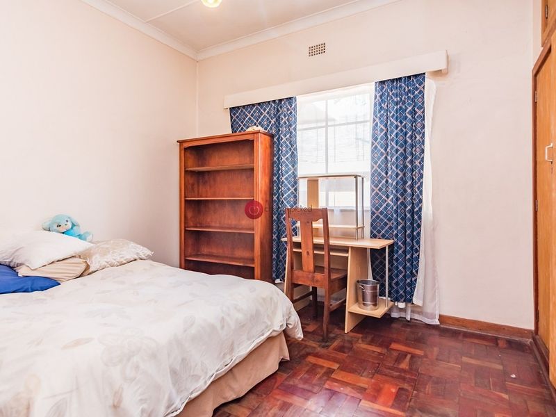 A bedroom featuring classic parquet flooring, a built-in cupboard, and a window with natural light.