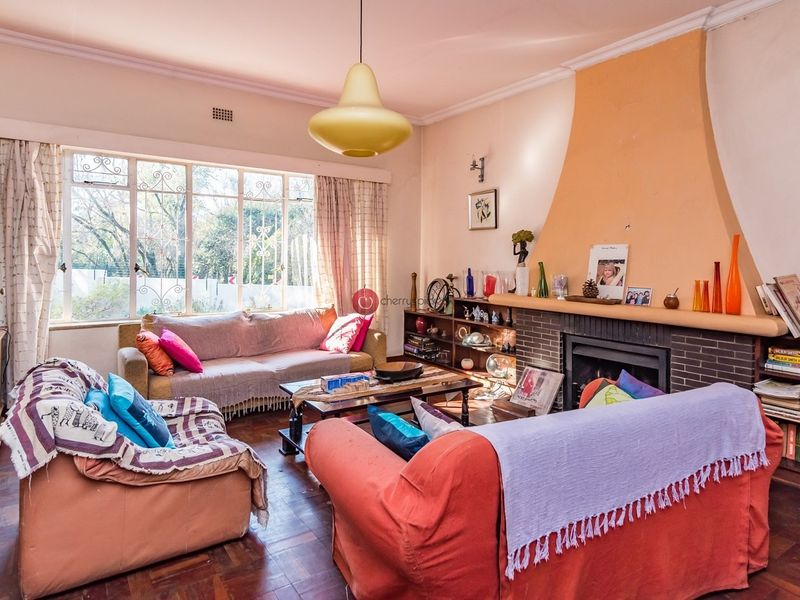 A cozy living room featuring original parquet flooring, a prominent brick fireplace with a decorative surround, and large windows providing natural light.