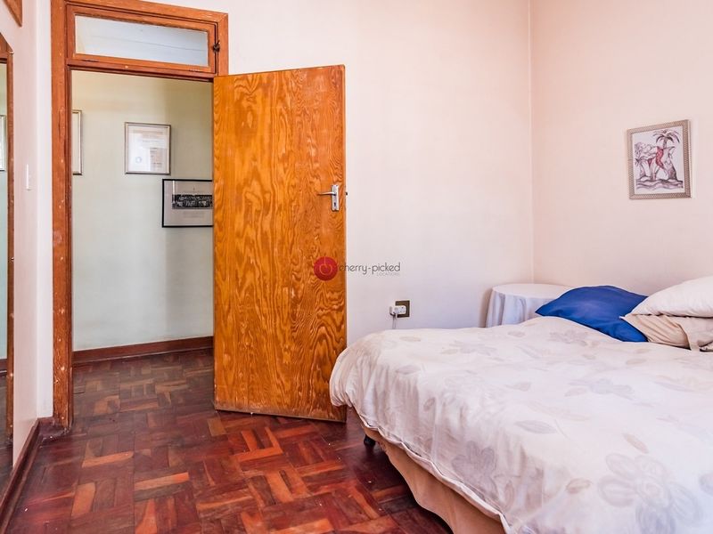 A bedroom featuring traditional parquet flooring and a wooden door with a transom window, offering a classic layout.