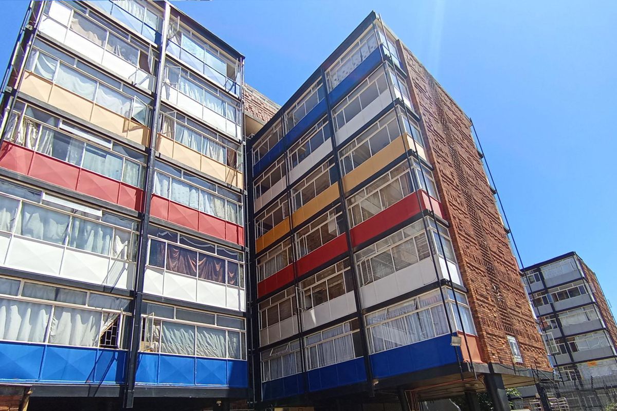 Exterior view of a multi-story apartment building featuring a distinctive colorful facade with metal-framed windows and brick detailing.