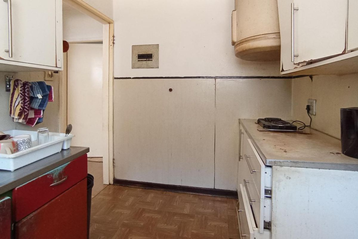 A dated kitchen featuring original cabinetry, laminate countertops, and an integrated extractor fan, requiring significant cosmetic updates and modernization.