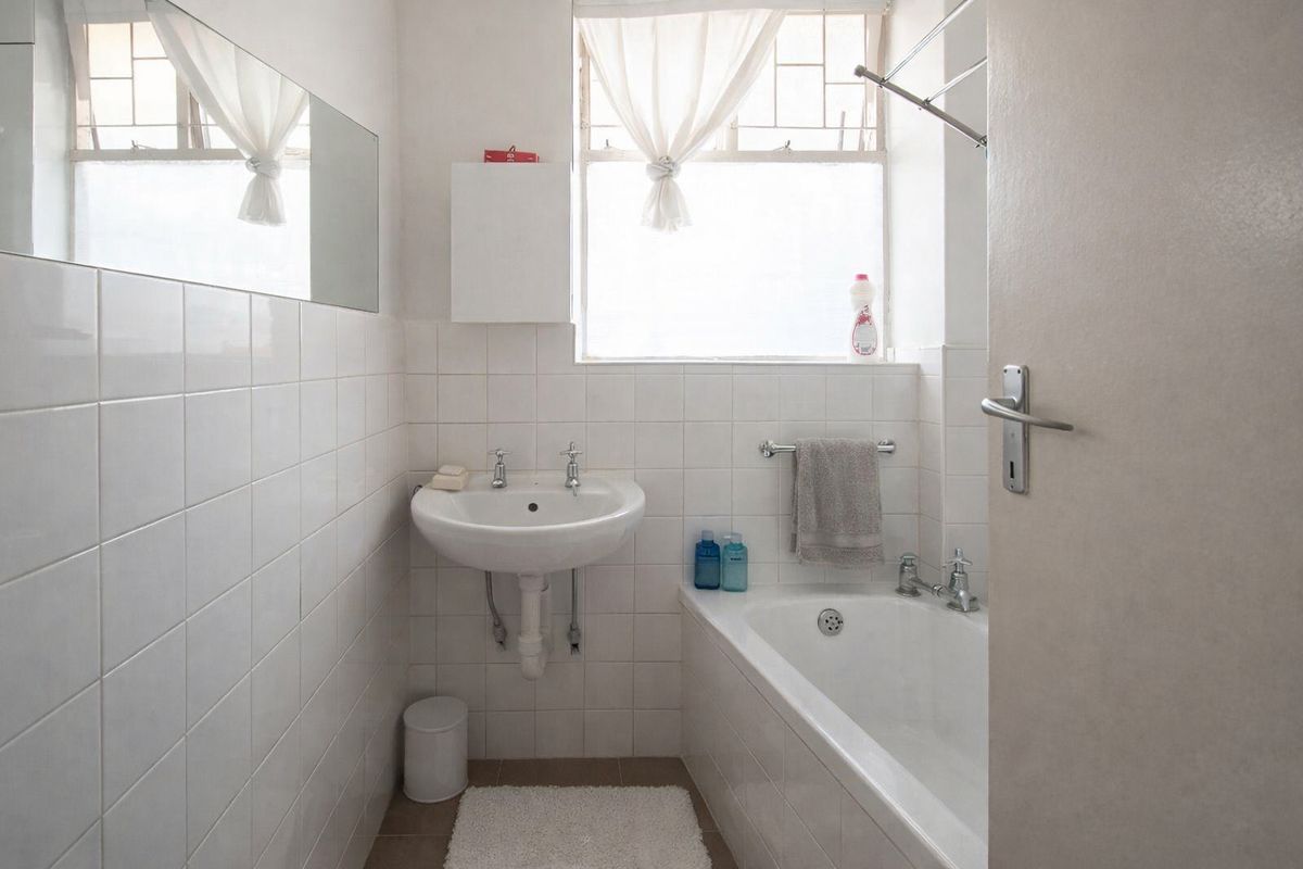 A compact bathroom featuring a wall-mounted basin, a built-in bathtub, and white wall tiling, offering a functional space with potential for modern updates.