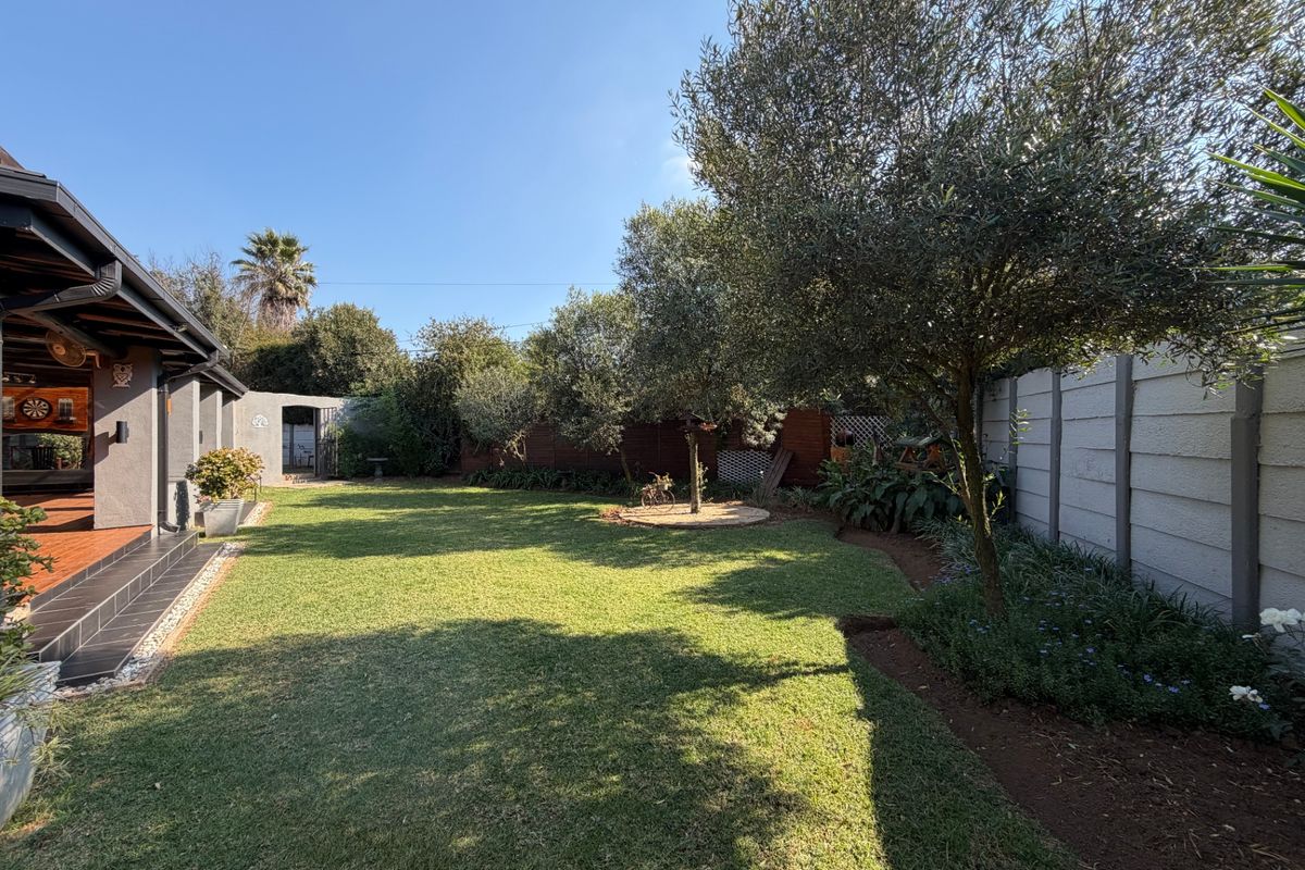 A well-maintained rear garden featuring a tiled patio, lush lawn, mature trees, and secure boundary walling, providing a private outdoor space.