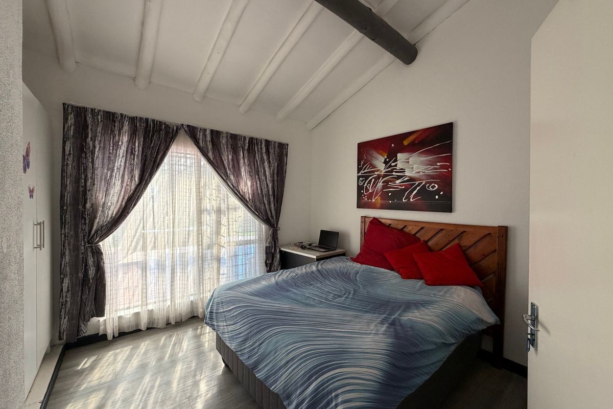 A bedroom featuring exposed ceiling beams, laminate flooring, and a built-in wardrobe, offering a cozy atmosphere with natural light.