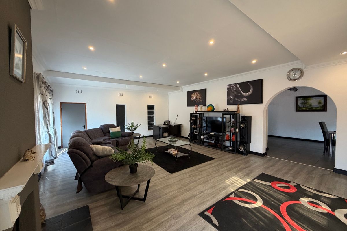 Spacious living room featuring modern laminate flooring, recessed downlighting, and a distinctive arched entryway leading to an adjacent area.