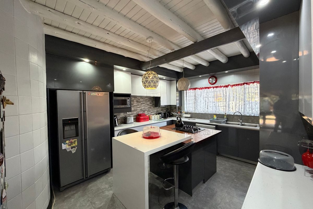 Modern kitchen featuring a central island, stone countertops, gas cooktop, built-in cabinetry, and distinctive exposed timber ceiling beams.