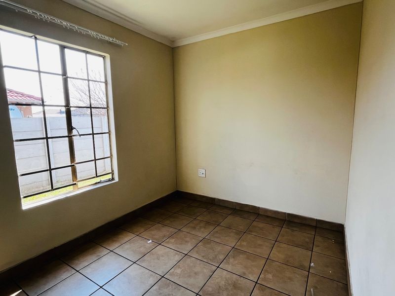 A vacant bedroom featuring tiled flooring, neutral walls, and a window fitted with security burglar bars.