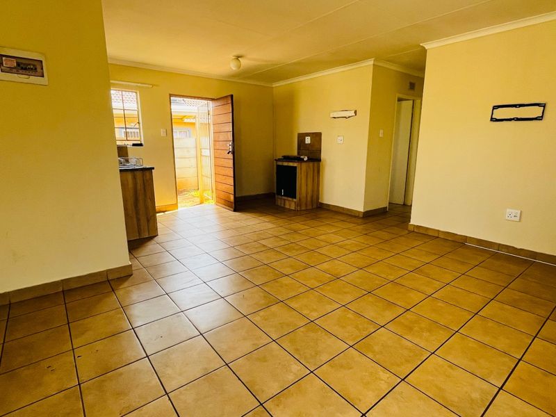 An open-plan living and kitchen area featuring tiled flooring, built-in cabinetry, and direct access to the exterior via a security gate.