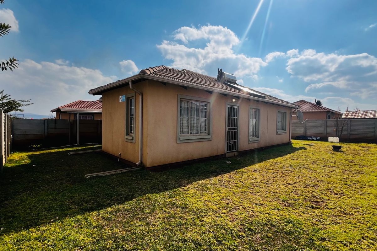 Rear view of a detached house featuring a tiled roof, solar geyser, and a surrounding precast concrete boundary wall with a grassed yard.