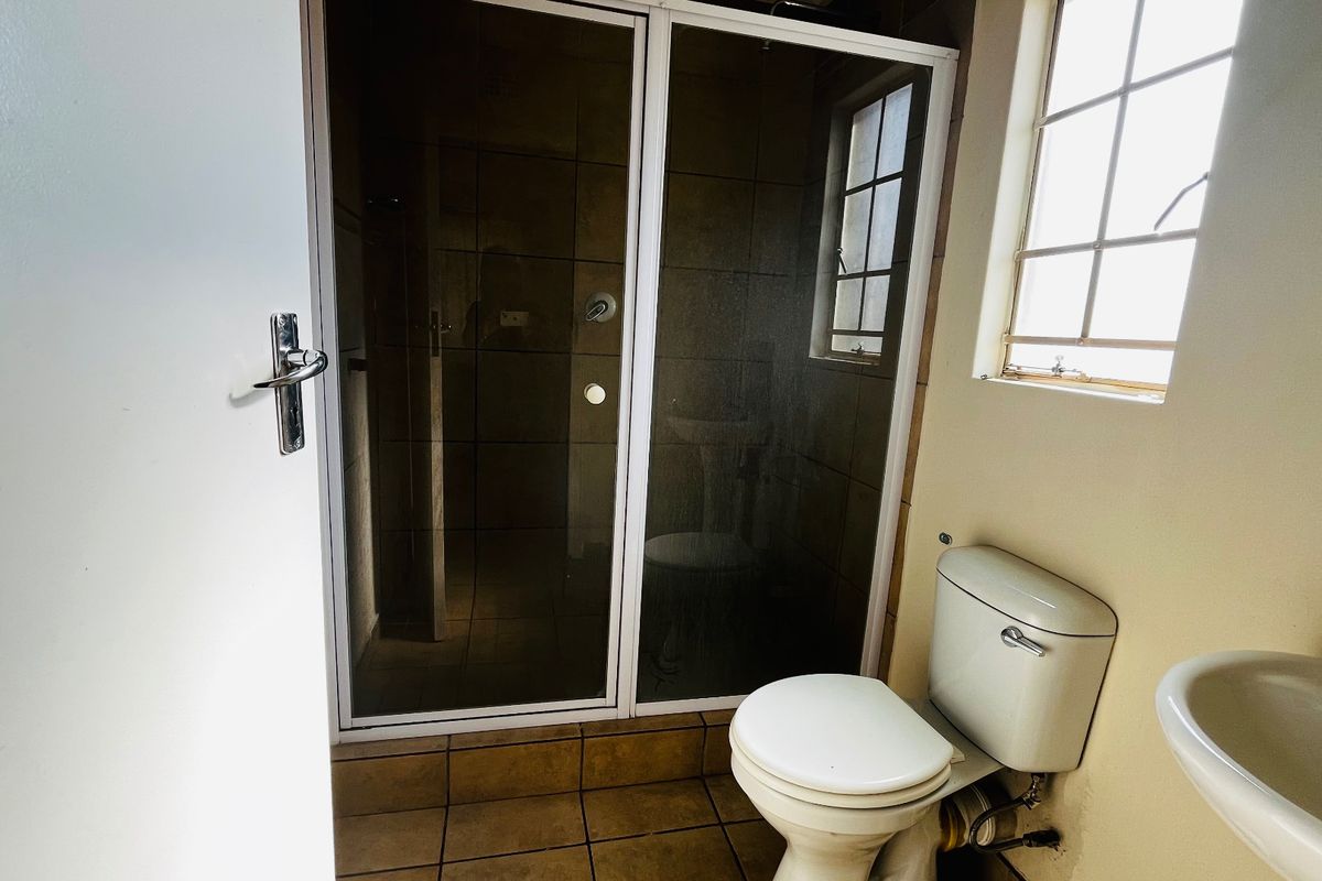 A functional bathroom featuring a shower enclosure, pedestal basin, and toilet, with tiled flooring and walls, ready for a modern update.