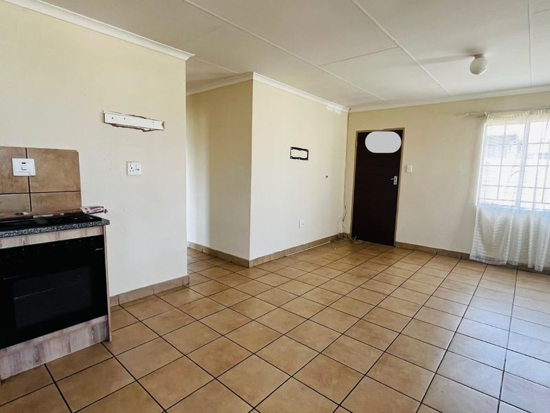 Open plan living area featuring tiled flooring, a freestanding oven, and security bars on the window. The space is vacant and ready for renovation.