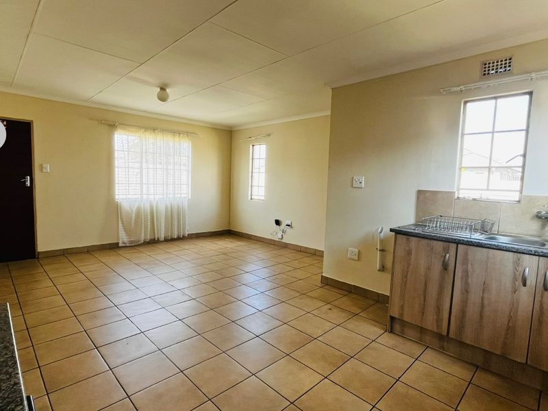 An open-plan living and kitchen area featuring tiled flooring, neutral walls, and basic kitchen cabinetry with a stainless steel sink.