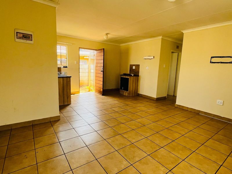 An open-plan living and kitchen area featuring ceramic floor tiles, built-in cabinetry, and direct access to the exterior via a security gate.