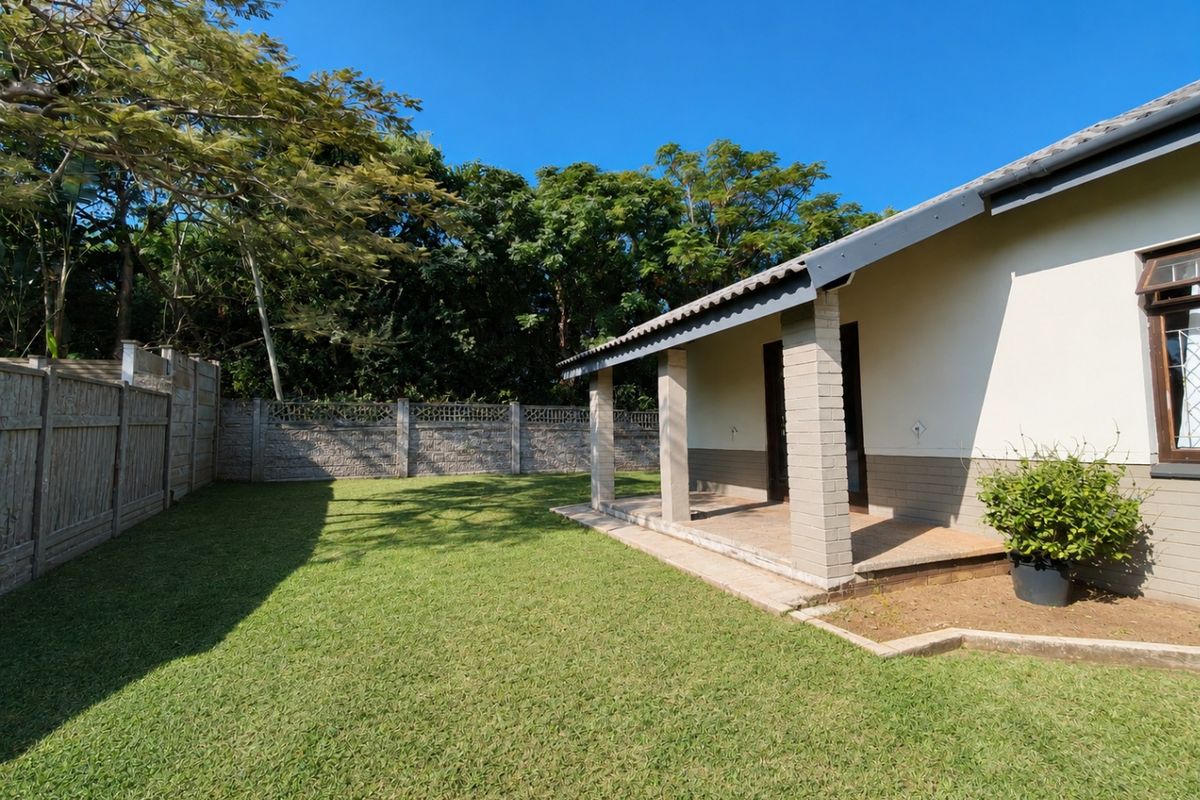 A well-maintained rear garden featuring a covered patio with brick pillars, a neat lawn, and secure precast concrete boundary walls.