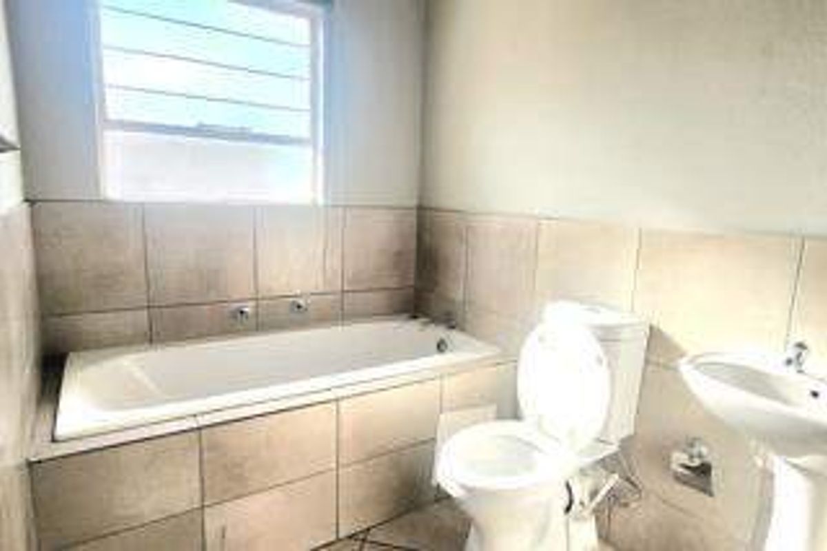 A functional bathroom featuring a built-in bathtub, pedestal basin, and toilet with neutral wall and floor tiling.