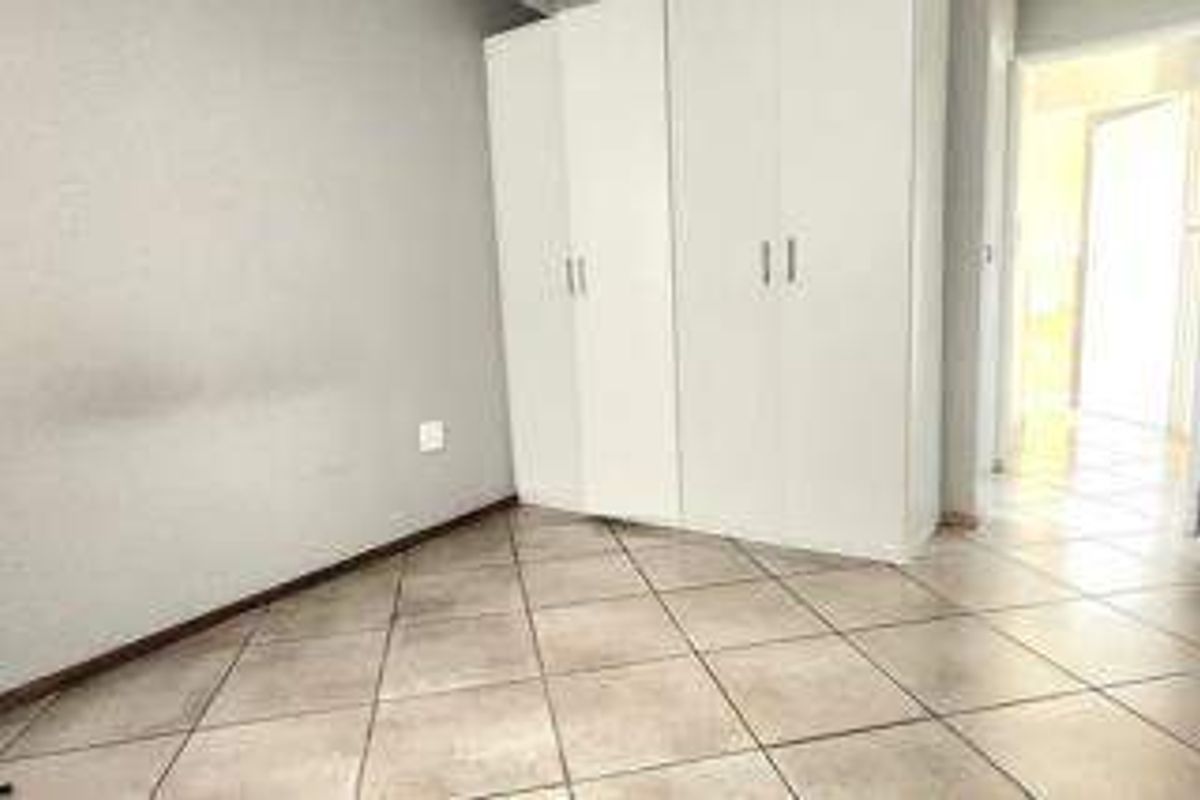 A vacant bedroom featuring neutral tiled flooring and built-in white cupboards, offering a clean and functional space ready for personalization.