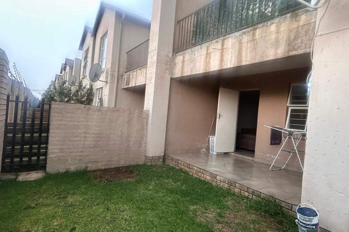 Rear exterior view of the townhouse featuring a small tiled patio, a private garden area, and a balcony with metal railings.