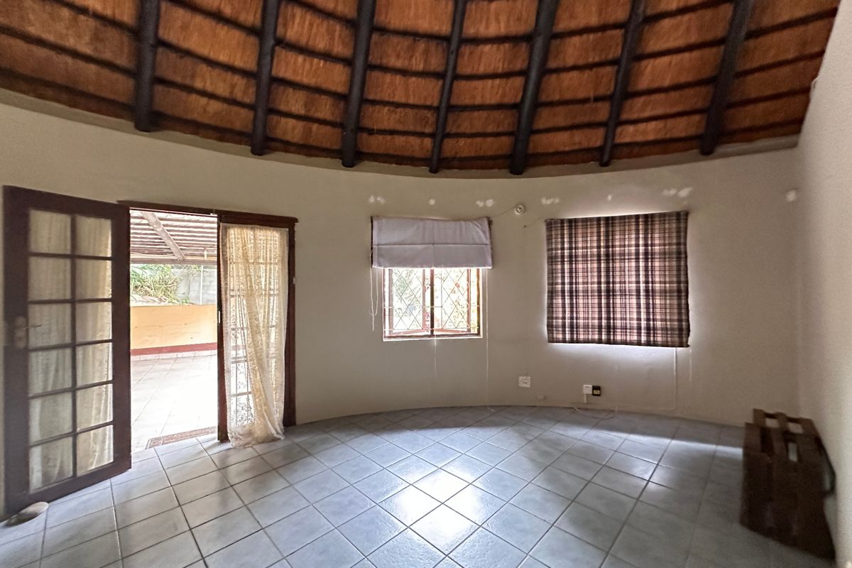 Spacious circular living area featuring a traditional thatched roof with exposed timber rafters, ceramic tiled flooring, and direct access to an outdoor patio.