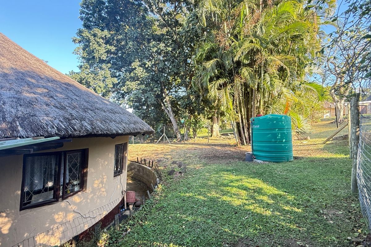 Rear exterior view of a townhouse featuring a traditional thatch roof, a green water storage tank, and a spacious garden area with mature trees.