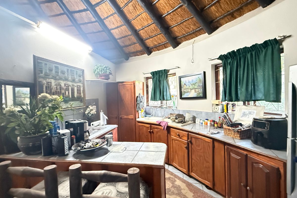 A rustic kitchen featuring a high thatched ceiling with exposed timber beams, wooden cabinetry, and tiled countertops in a traditional townhouse setting.