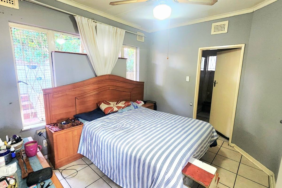 A bedroom featuring tiled flooring, a ceiling fan, and security bars on the windows, with an attached doorway leading to an adjacent room.