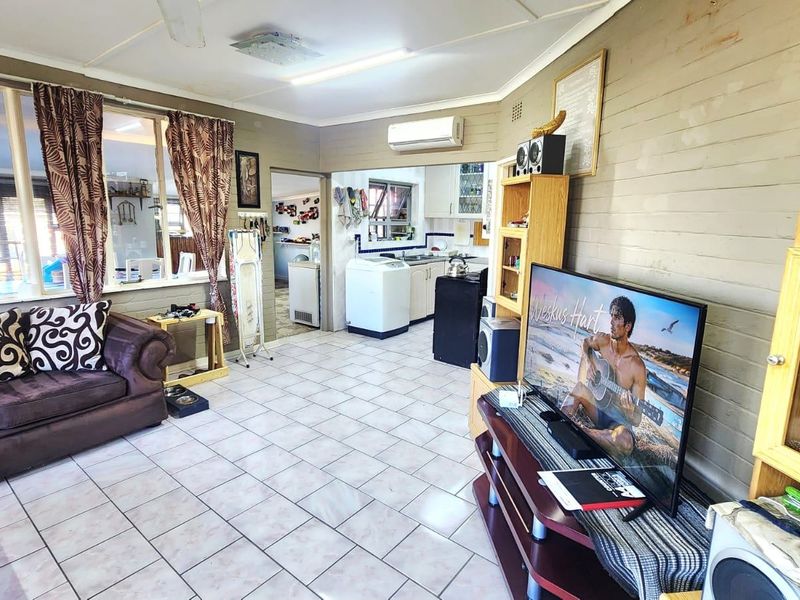 Open-plan living area featuring tiled flooring, a split-system air conditioner, and a ceiling fan, with an adjacent view into the kitchen and laundry area.