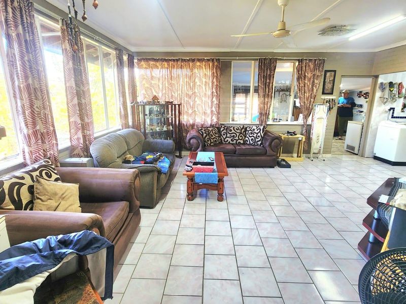 Spacious living area featuring tiled flooring, a ceiling fan, and a wall-mounted air conditioning unit, with large windows providing ample natural light.