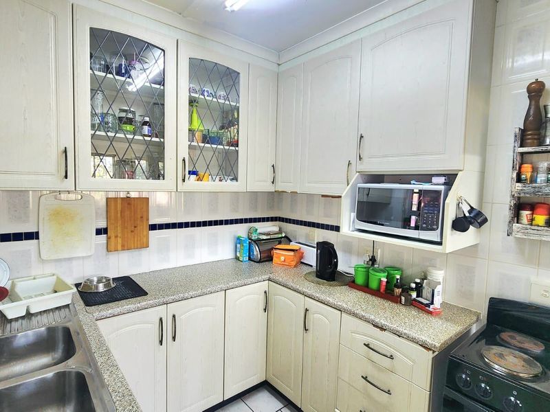 A functional kitchen featuring laminate cabinetry, granite countertops, a double bowl stainless steel sink, and built-in microwave housing with classic tiled splashbacks.