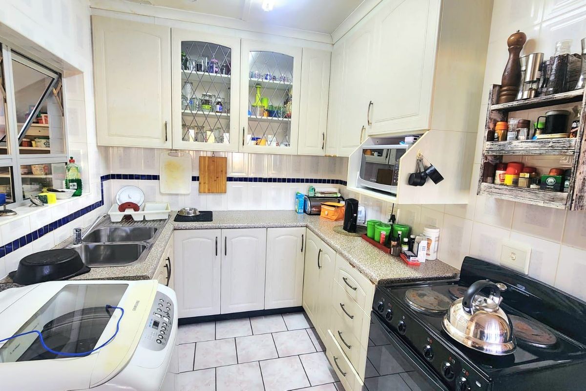 A functional U-shaped kitchen featuring light-toned cabinetry, tiled backsplash, double basin sink, and ceramic floor tiles, offering a practical layout for daily use.