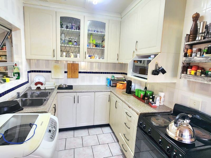 A functional U-shaped kitchen featuring light-toned cabinetry, tiled backsplash, double basin sink, and ceramic floor tiles, offering a practical layout for daily use.