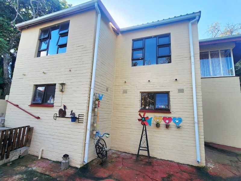 Rear exterior view of the townhouse featuring a painted brick facade, aluminium windows, and a paved courtyard area with external staircase access.