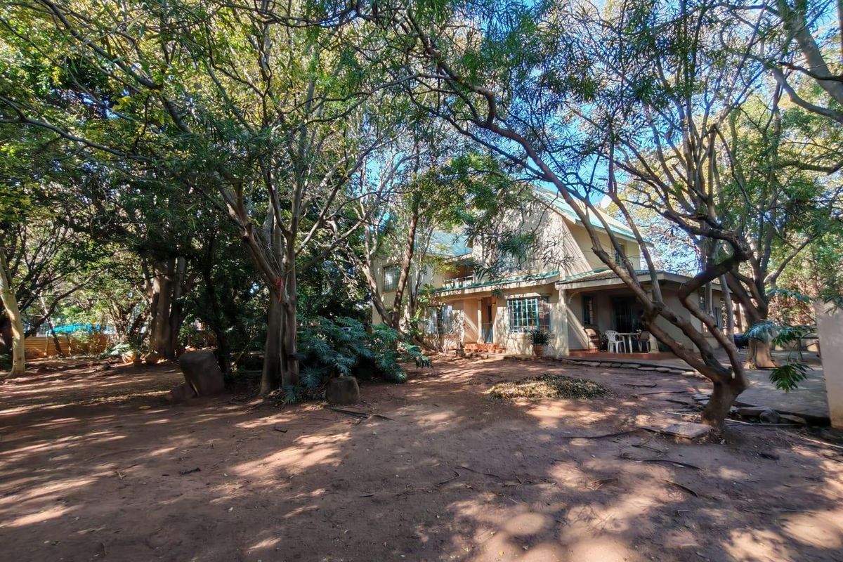 Rear view of the house featuring a covered patio area set within a large, mature garden with extensive tree coverage.