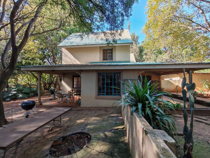 Rear view of a two-story house featuring a covered patio, paved courtyard area, and mature surrounding trees.