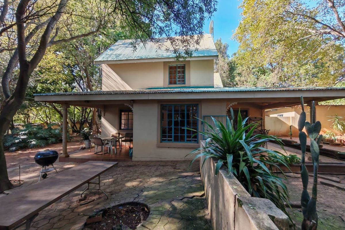 Rear view of a two-story house featuring a covered patio, paved courtyard area, and mature surrounding trees.