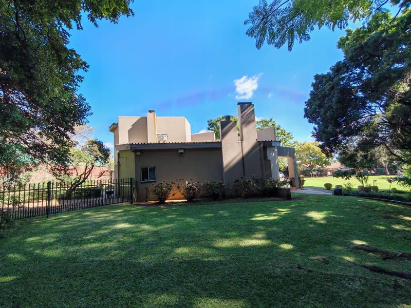 A view of the rear elevation of the house featuring a chimney, paved patio area, and a well-maintained garden enclosed by a metal fence.