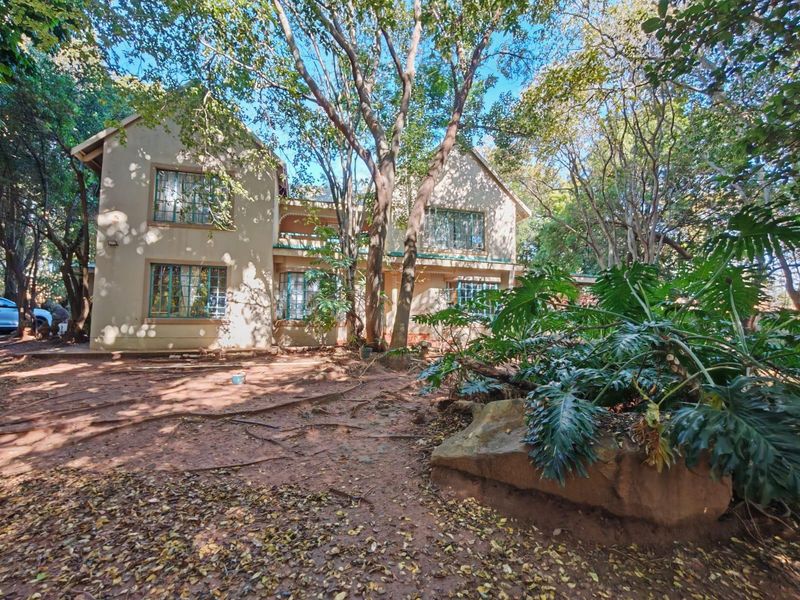 Rear view of a two-story residential property featuring a balcony, security bars on windows, and a mature, heavily wooded garden setting.