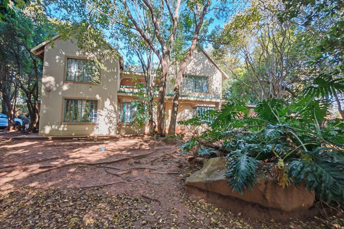 Rear view of a two-story residential property featuring a balcony, security bars on windows, and a mature, heavily wooded garden setting.