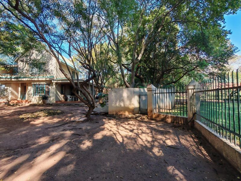 Rear garden area featuring mature trees, a covered patio, and perimeter metal fencing with a masonry boundary wall.