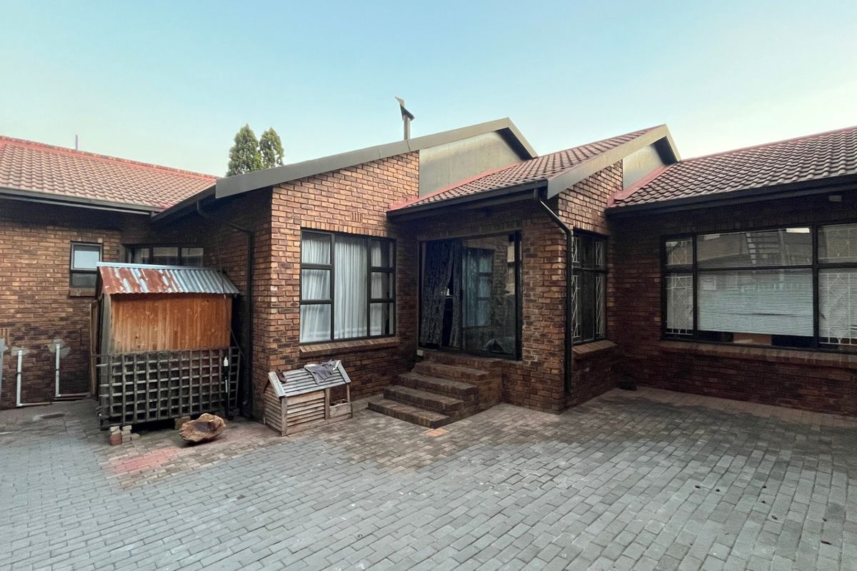 Rear view of a face-brick townhouse featuring a paved courtyard, tiled roof, and aluminium-framed windows with a sliding door entrance.