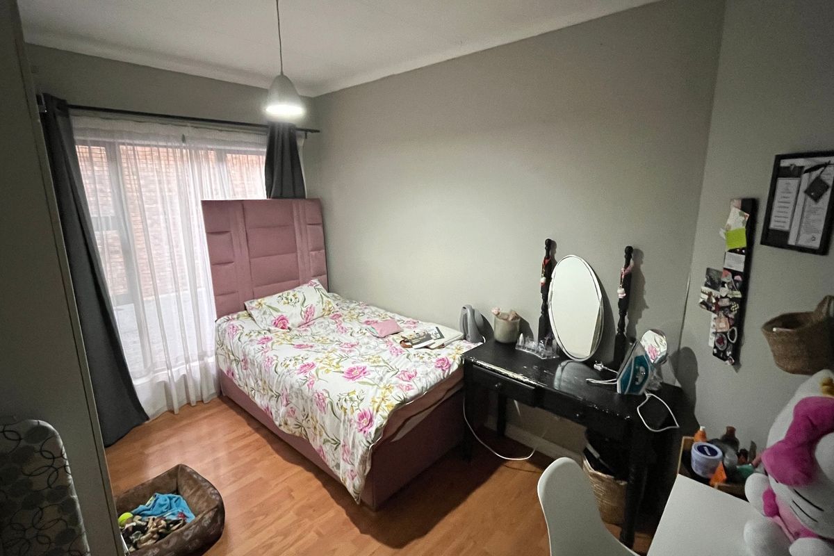 A functional bedroom featuring laminate flooring, neutral wall tones, and a pendant light fixture, offering a comfortable space with natural light access.