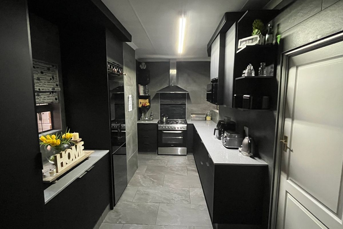 Modern galley-style kitchen featuring sleek dark cabinetry, stone countertops, stainless steel appliances, and contemporary floor tiling.