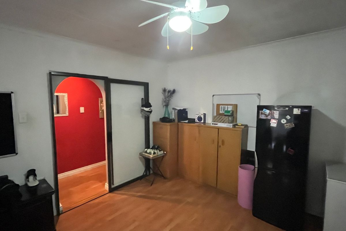 A living area featuring laminate flooring, a ceiling fan, and an arched doorway leading to an adjacent room.