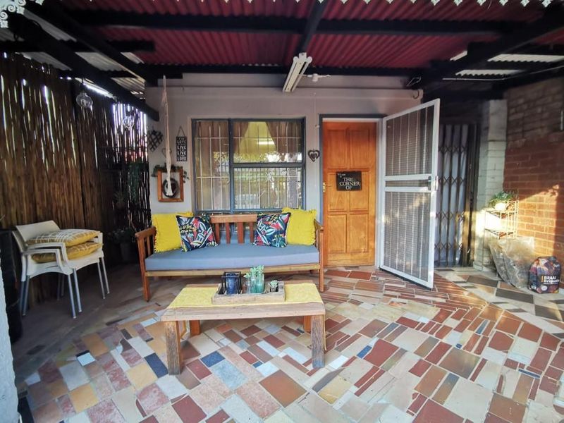 A covered outdoor patio area featuring a corrugated metal roof, tiled flooring, and a secure timber entrance door.