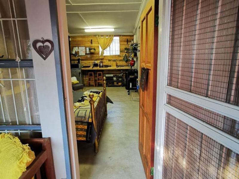View through a security screen door into an open-plan living and kitchen area featuring timber wall paneling and concrete flooring.