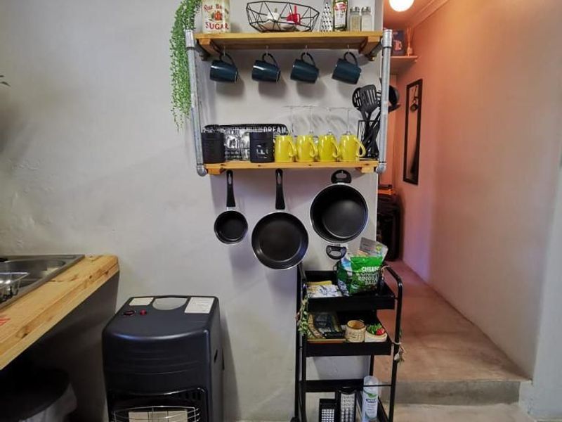 A functional kitchen area featuring a stainless steel sink, wooden countertop, and wall-mounted shelving for storage, leading into a hallway.