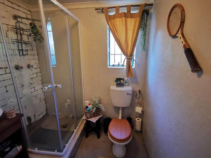 A compact bathroom featuring a shower enclosure, toilet, and an exposed brick wall finish, requiring some cosmetic updates to improve the overall aesthetic.