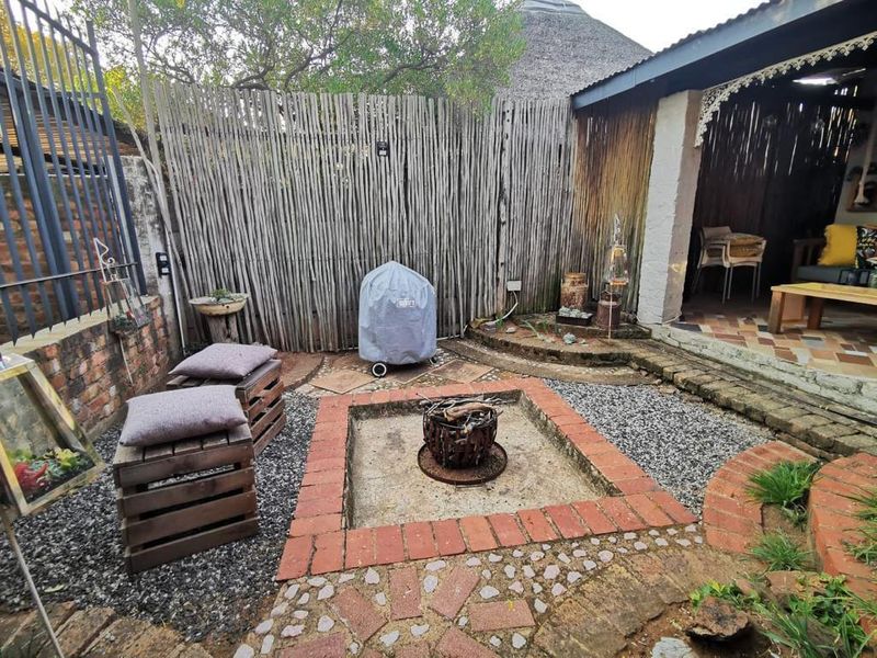 Outdoor entertainment area featuring a built-in brick fire pit, paved surrounds, and a covered patio section with a traditional thatched roof.
